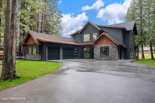view of front of house featuring aphalt driveway, roof with shingles, a front yard, stone siding, and a garage