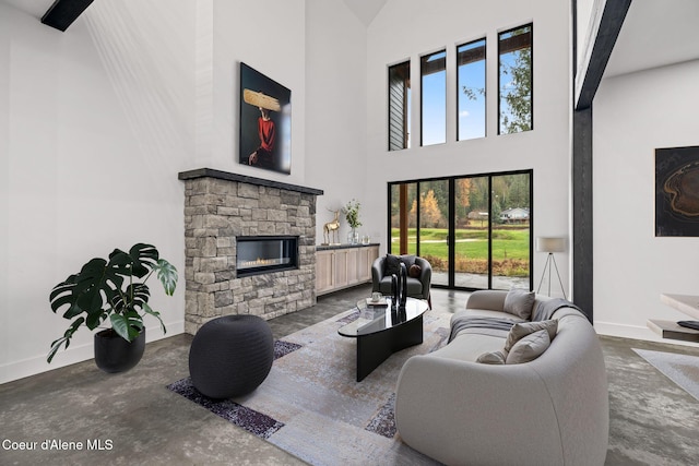 living area featuring a stone fireplace, a high ceiling, and baseboards