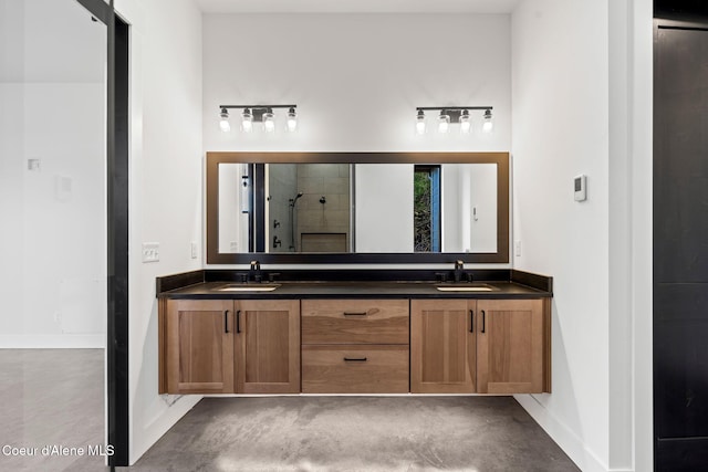 full bath with a tile shower, double vanity, a sink, and baseboards