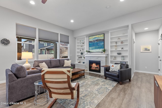 living room featuring built in features, light hardwood / wood-style flooring, ceiling fan, and a tiled fireplace