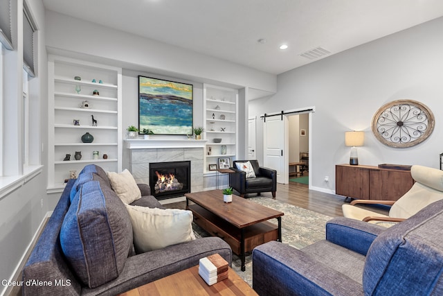 living room with a tile fireplace, wood-type flooring, a barn door, and built in shelves