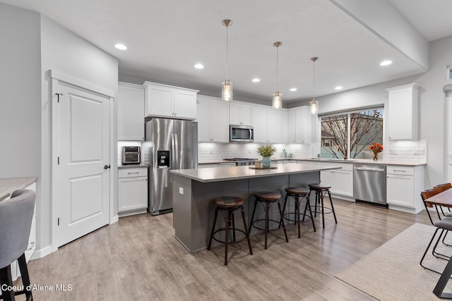 kitchen with appliances with stainless steel finishes, light wood-type flooring, decorative light fixtures, and white cabinetry