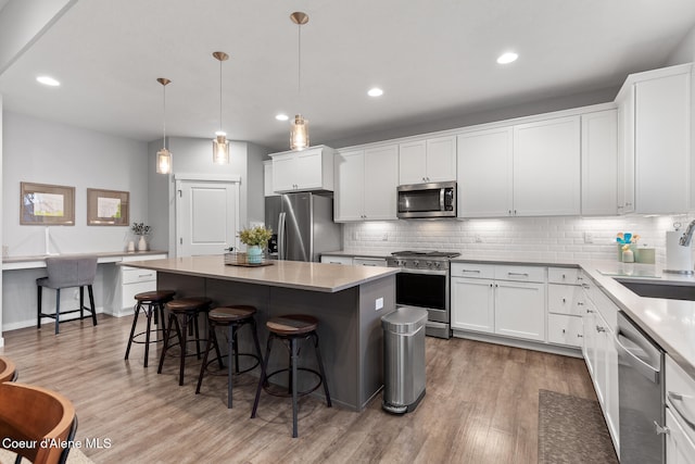 kitchen featuring stainless steel appliances, light hardwood / wood-style flooring, pendant lighting, a kitchen bar, and a kitchen island