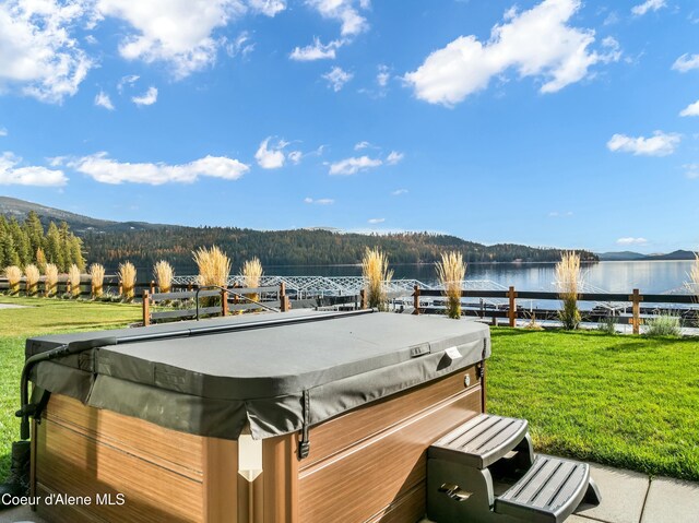 wooden terrace featuring a hot tub, a water and mountain view, and a lawn