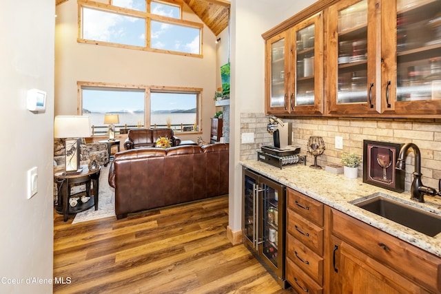 kitchen with light stone countertops, backsplash, beverage cooler, sink, and hardwood / wood-style flooring