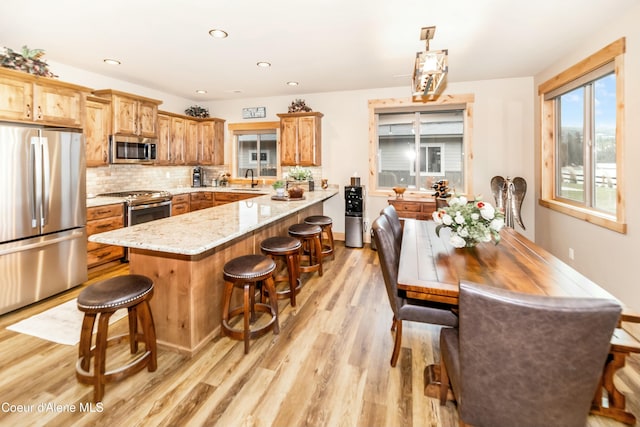 kitchen with pendant lighting, a breakfast bar, light stone countertops, light wood-type flooring, and appliances with stainless steel finishes