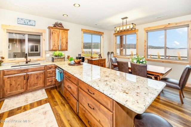 kitchen featuring hardwood / wood-style floors, backsplash, a water view, sink, and hanging light fixtures