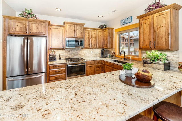 kitchen with light stone countertops, appliances with stainless steel finishes, backsplash, a kitchen breakfast bar, and sink