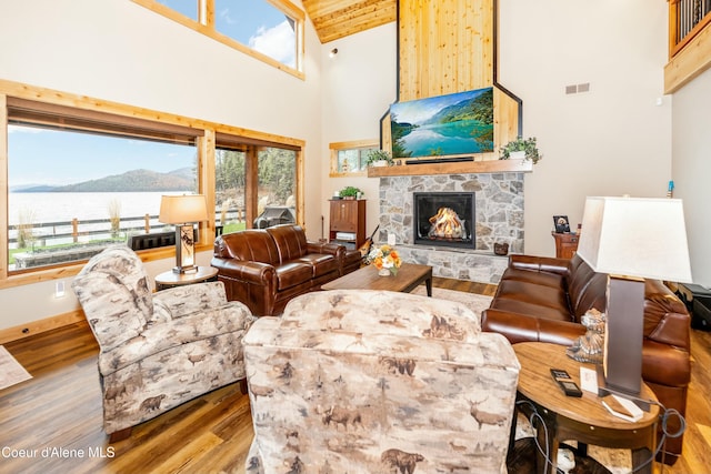 living room with a water view, a stone fireplace, high vaulted ceiling, and hardwood / wood-style flooring