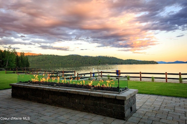 patio terrace at dusk featuring a lawn, a water and mountain view, and a boat dock