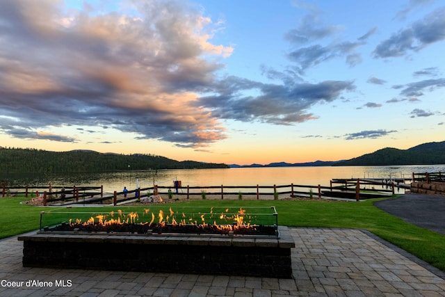 patio terrace at dusk with a boat dock, a water and mountain view, and a lawn