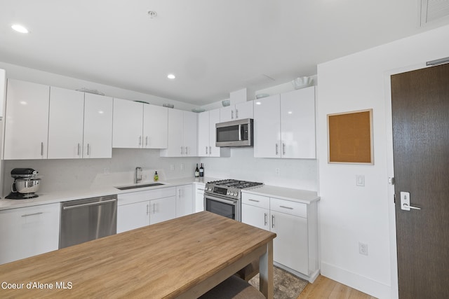 kitchen with light hardwood / wood-style flooring, stainless steel appliances, white cabinetry, and sink