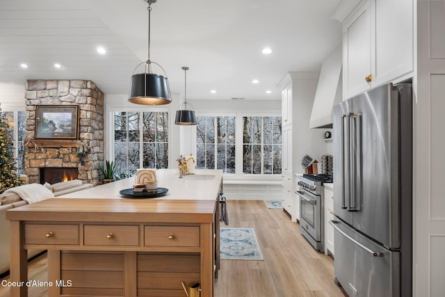 kitchen featuring white cabinetry, premium appliances, decorative light fixtures, a fireplace, and light wood-type flooring