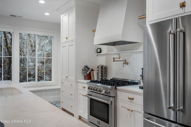 kitchen with white cabinetry, sink, light stone countertops, custom range hood, and high end appliances