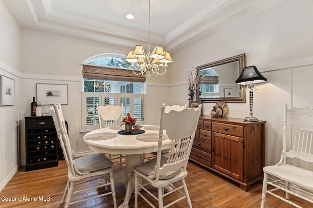 dining area with hardwood / wood-style flooring, a notable chandelier, a raised ceiling, and crown molding