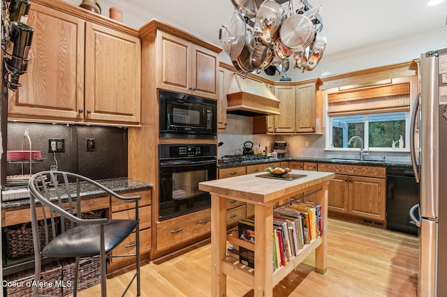 kitchen with black appliances, crown molding, sink, light wood-type flooring, and custom range hood