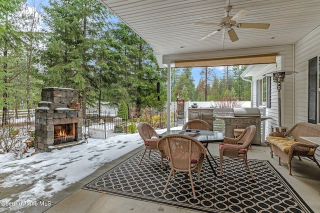 snow covered patio featuring an outdoor stone fireplace, area for grilling, and ceiling fan