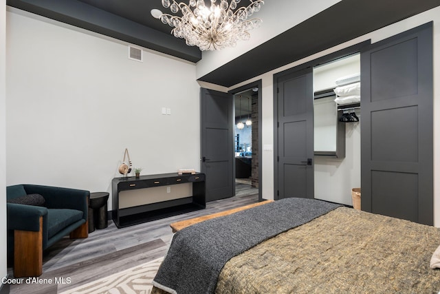 bedroom featuring visible vents, ensuite bath, wood finished floors, an inviting chandelier, and a closet