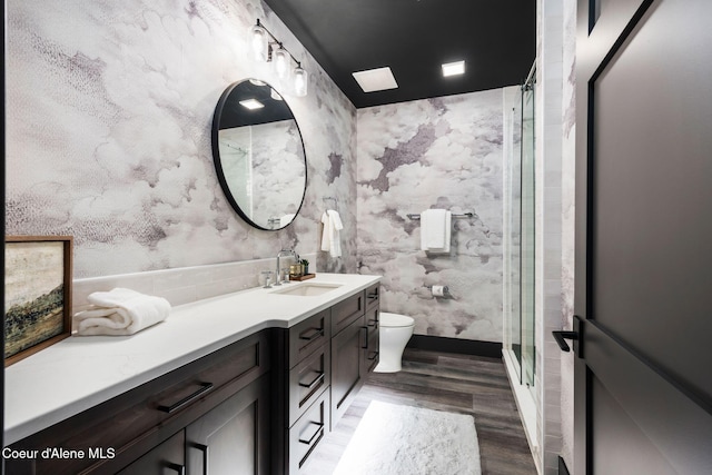 full bathroom featuring a shower with door, toilet, vanity, wood finished floors, and wallpapered walls