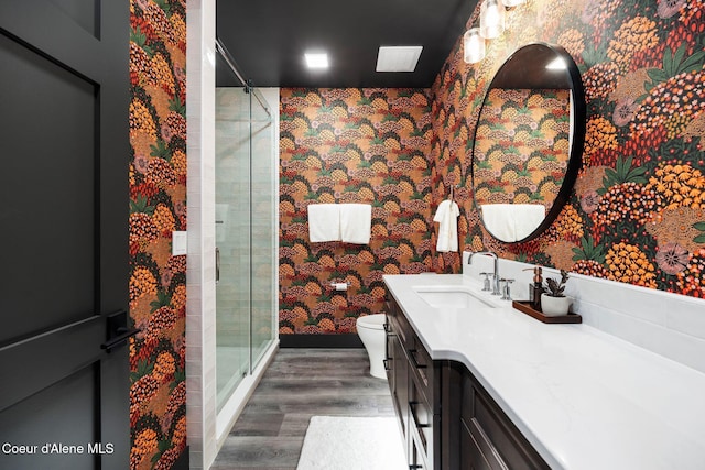 bathroom featuring wallpapered walls, toilet, wood finished floors, vanity, and a shower stall