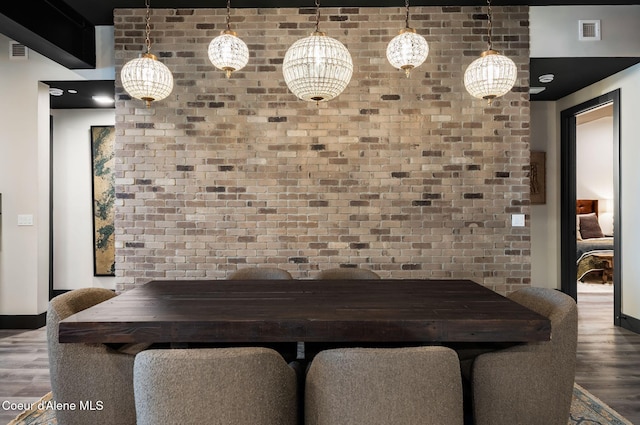unfurnished dining area with brick wall, an accent wall, visible vents, and wood finished floors