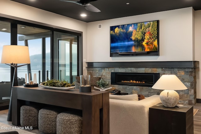 living area featuring visible vents, wood finished floors, a ceiling fan, and a stone fireplace