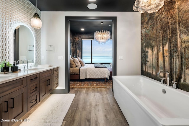ensuite bathroom with connected bathroom, wood finished floors, a sink, a freestanding bath, and double vanity