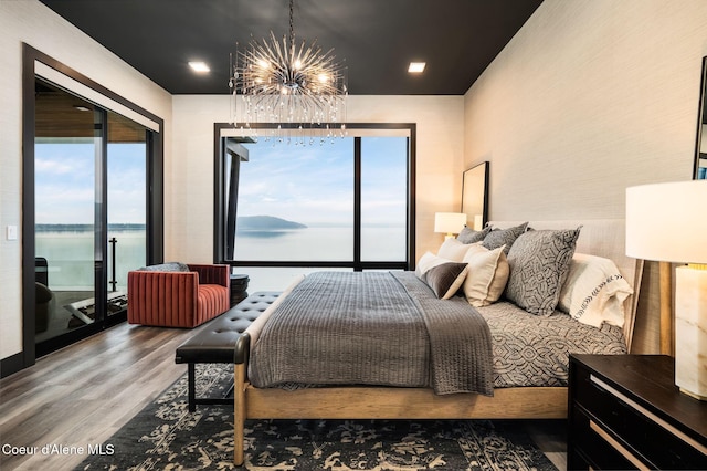 bedroom featuring access to exterior, a chandelier, a water view, and wood finished floors