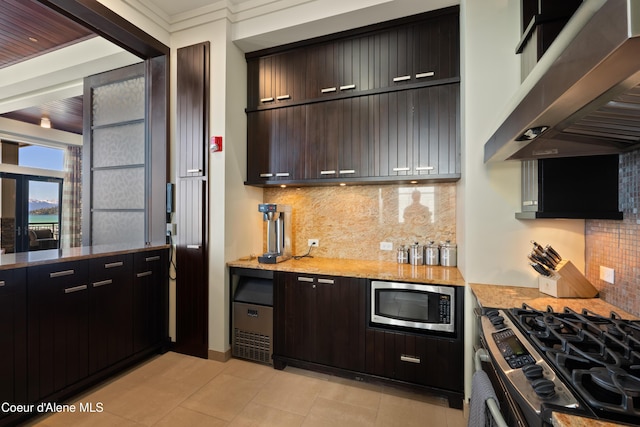 kitchen featuring light stone counters, stainless steel appliances, decorative backsplash, dark brown cabinets, and under cabinet range hood