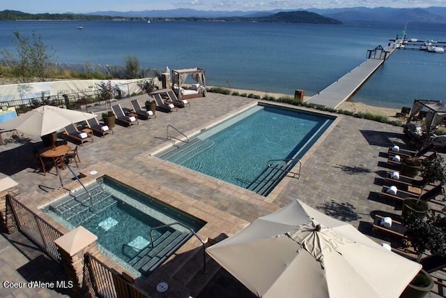 community pool featuring a patio area, a water view, fence, and a hot tub