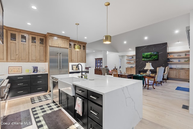 kitchen featuring light stone countertops, sink, a center island with sink, light hardwood / wood-style floors, and hanging light fixtures