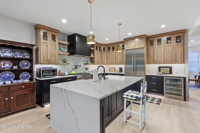 kitchen with a center island with sink, wine cooler, light stone countertops, light wood-type flooring, and stainless steel appliances