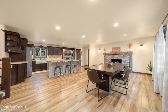 dining room with a stone fireplace, light hardwood / wood-style flooring, and sink