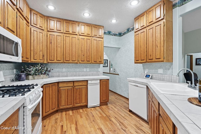 kitchen with light wood-type flooring, a textured ceiling, white appliances, sink, and tile counters