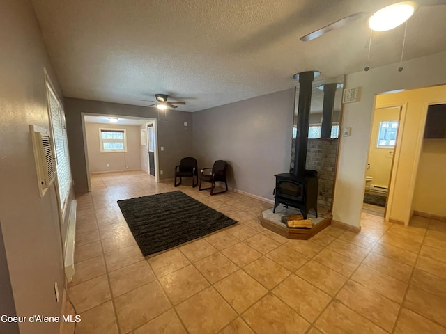 unfurnished living room featuring ceiling fan, light tile patterned flooring, a wood stove, and a textured ceiling