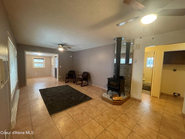 unfurnished living room featuring a wood stove, ceiling fan, light tile patterned floors, and a textured ceiling