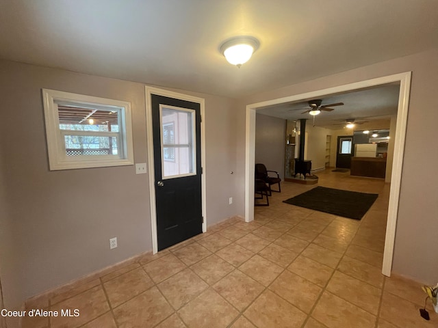 entrance foyer featuring ceiling fan, a wood stove, and light tile patterned floors