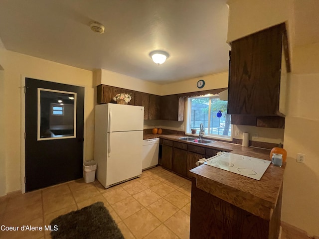 kitchen with dark brown cabinetry, white appliances, sink, and light tile patterned floors