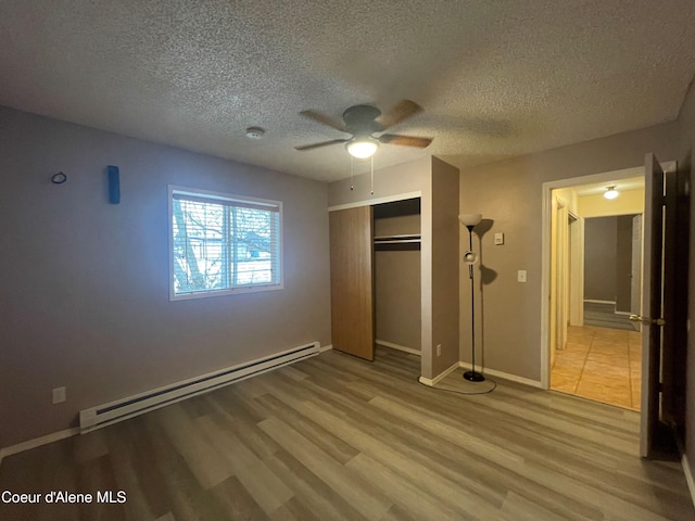 unfurnished bedroom featuring a baseboard heating unit, ceiling fan, a textured ceiling, light hardwood / wood-style floors, and a closet