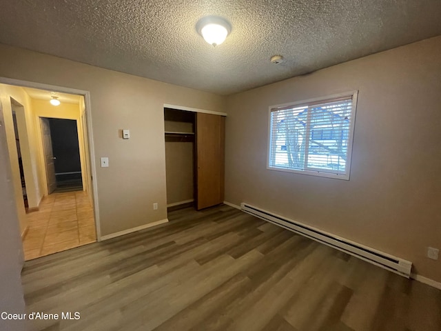 unfurnished bedroom featuring baseboard heating, a closet, wood-type flooring, and a textured ceiling