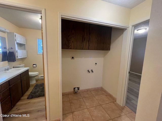 clothes washing area with cabinets, a baseboard radiator, electric dryer hookup, light hardwood / wood-style flooring, and hookup for a washing machine