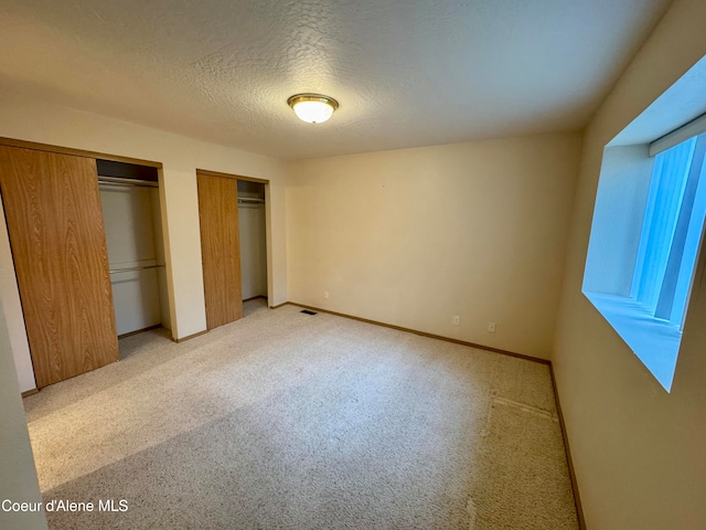 unfurnished bedroom with light colored carpet, a textured ceiling, and multiple closets