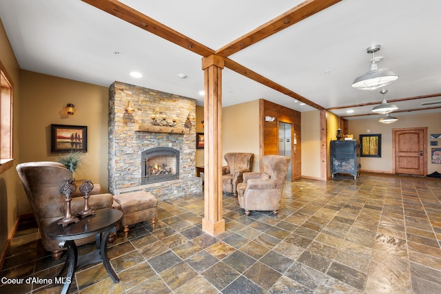 living room with beamed ceiling, a stone fireplace, and decorative columns