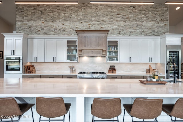 kitchen with decorative backsplash, white cabinetry, stainless steel appliances, and a large island with sink