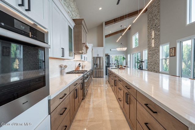 kitchen with high vaulted ceiling, sink, appliances with stainless steel finishes, decorative light fixtures, and white cabinetry