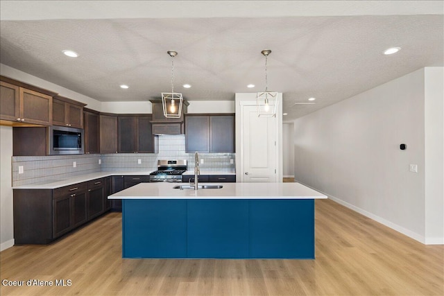 kitchen featuring a kitchen island with sink, light hardwood / wood-style flooring, stainless steel appliances, and decorative light fixtures