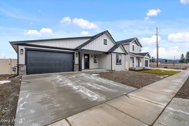 view of front facade with a garage, concrete driveway, stone siding, fence, and board and batten siding