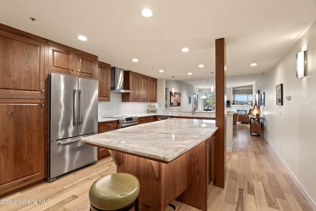 kitchen with wall chimney range hood, a breakfast bar area, light hardwood / wood-style flooring, kitchen peninsula, and stainless steel appliances