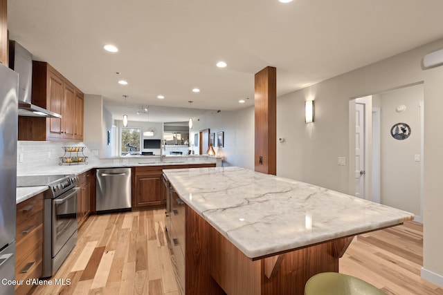 kitchen with a kitchen bar, decorative backsplash, stainless steel appliances, a center island, and light hardwood / wood-style floors