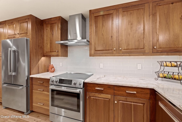 kitchen with wall chimney range hood, decorative backsplash, light stone countertops, light wood-type flooring, and stainless steel appliances